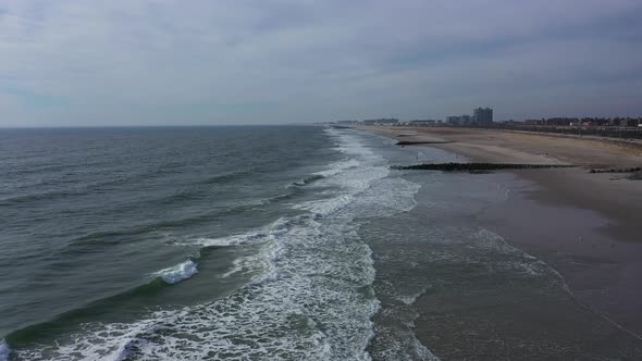 A drone view of an empty beach on a cloudy day. The camera dolly in over the gentle waves of the oce