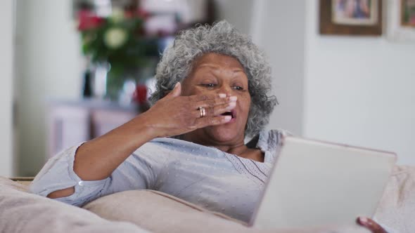 Senior african american woman waving and blowing kisses while having a video call on digital tablet