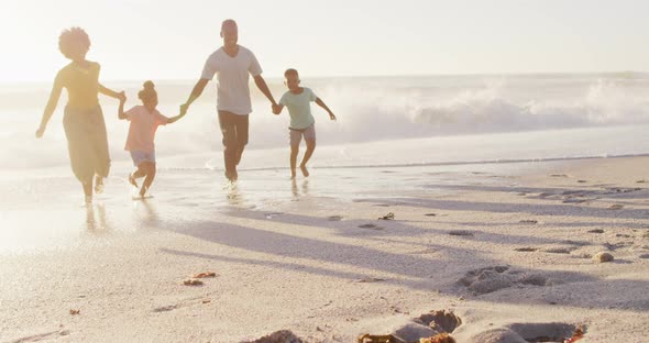 Smiling african american family walking and holding hands on sunny beach