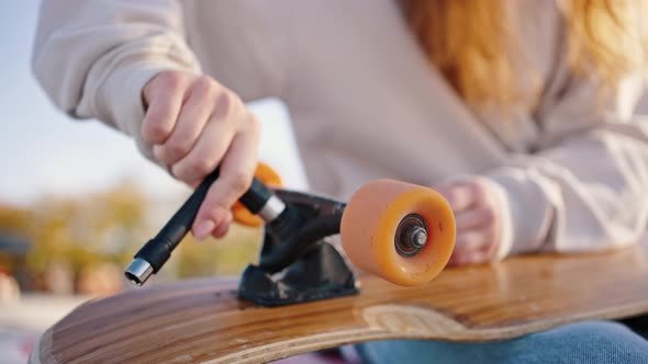Close Up of Unrecognizable Skateboarder Girl Unscrewing Wheels on Her Longboard with Allen Key or