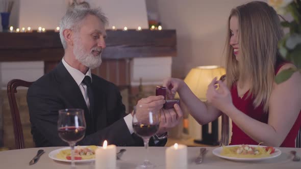 Confident Senior Man Making Marriage Proposal To Young Woman During Romantic Dinner. Excited Girl