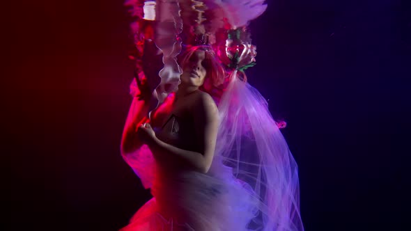 a Woman with Long Hair Floats in the Dark Water. She Presses a Huge Flower To Her Face. Reflection