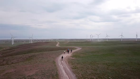 A Group of Cyclists Rides Along the Windmills