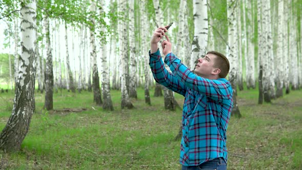 A Young Man Is Looking for a Cellular Network in a Birch Forest. A Man Is Talking on the Phone, but