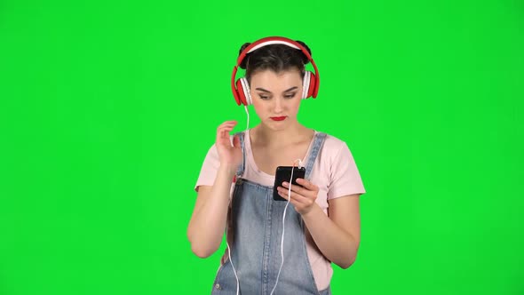 Girl in Big Red Headphones Chooses Music on Mobile Phone on Green Screen