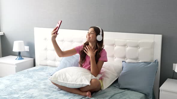Happy Child in Headphones Making Video Selfie on Mobile Phone Relaxing in Bed Modern Education