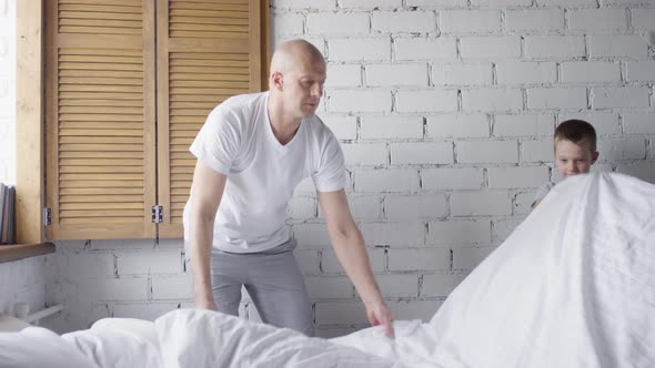 Man and Schoolboy Making Bed in Morning