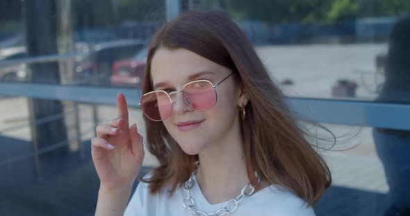 Portrait of Stylish Young Girl Smiling at Camera When Correcting Sunglasses