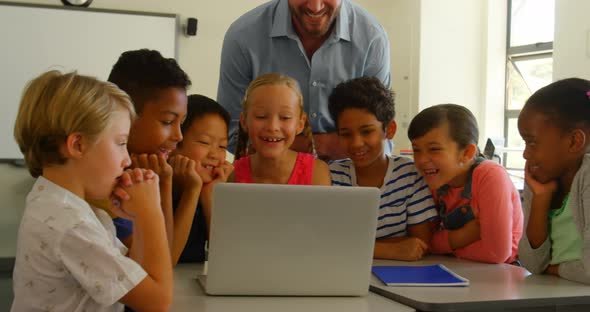 Adult Caucasian male teacher teaching kids on laptop in classroom at school 4k