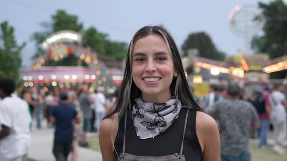 Push in to young woman standing and smiling at a carnival