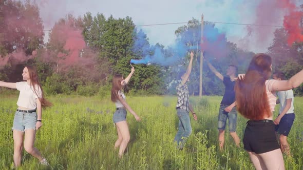 Cheerful Friends Spray Colored Smoke on a Meadow in Summer