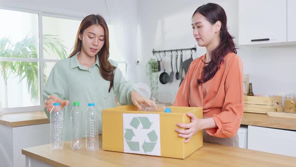 Asian young woman friend put plastic bottles into recycle box, separate trash for recycling at home.