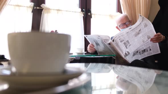 Old Grandfather Reads a Newspaper Sitting in a Cafe
