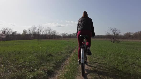 Young Woman on a Bicycle Rides Along a Path in the Forest in a Sunny Spring Day