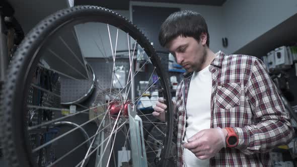 A Man is a Bicycle Mechanic Repairing a Wheel in a Bike Store Workshop