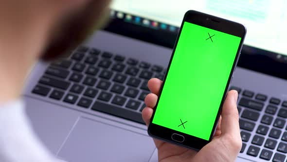 A Black Smartphone with Green Screen for Chroma Key Compositing the Hands of a Man on Laptop