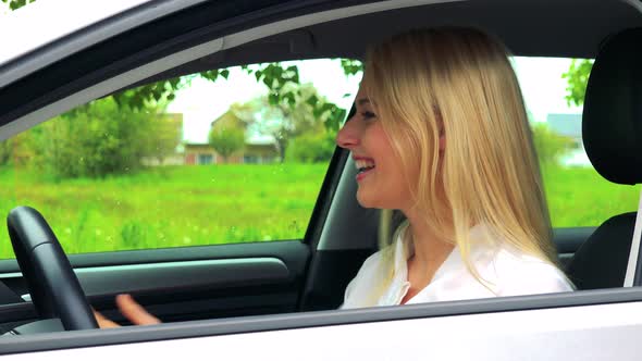 Young Attractive Blond Woman Sits in the Car and Rajoices