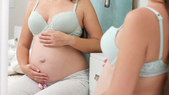 Beautiful Pregnant Woman in Bra with Big Belly Sitting at Mirror and Looking in Reflection on Her