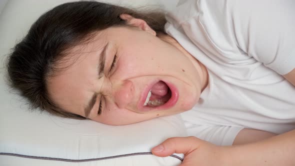 A 30Yearold Brunette Woman Yawns Lying on a Pillow on Her Bed