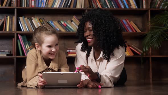 Schoolgirl and Babysitter Look at Tablet Display and Laugh
