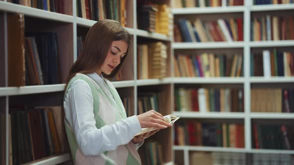 Female reader standing by bookcase and reading book