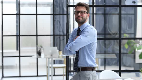 Smiling young happy businessman looking at camera standing at office
