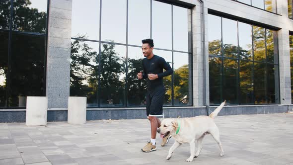 Young Black Man Running with His White Labrador Dog in Buseness City Center During Beautiful Fall