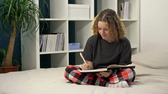 Cute Teenage Girl Doing Homework Sitting on the Bed at Home