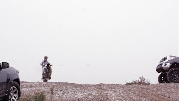 Two motorcycles jumping over hill between two SUVs.