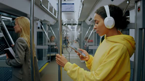 Young Girl Standing in Metro Train Wearing Headphones and Looking in Her Phone