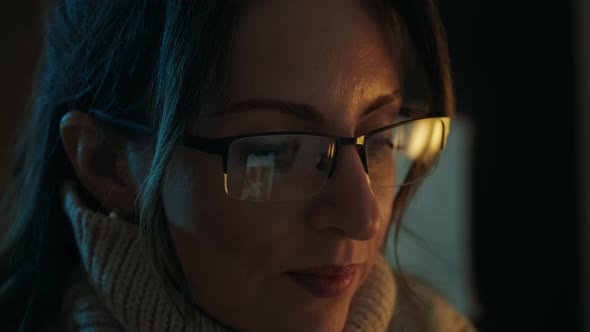 Pretty woman in eyeglasses late at night scrolling with smartphone