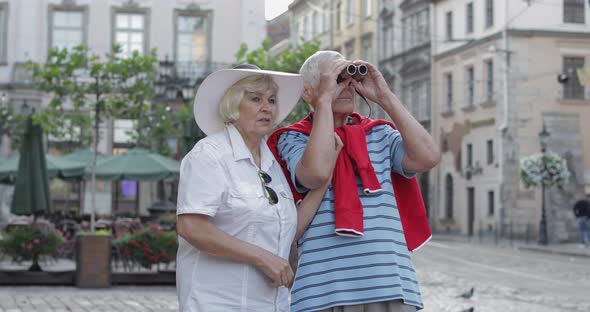 Senior Male and Female Tourists Walking in Town Center and Looking in Binoculars