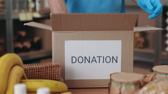 Close Up of Volunteer in Gloves Packing Food in Donation Box