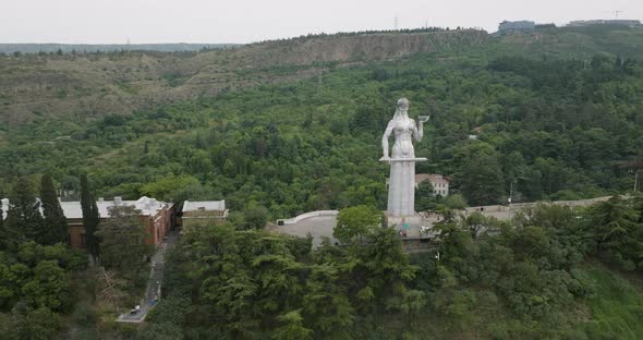 Arc aerial shot of the Kartlis Deda statue and a beautiful Tbilisi landscape.