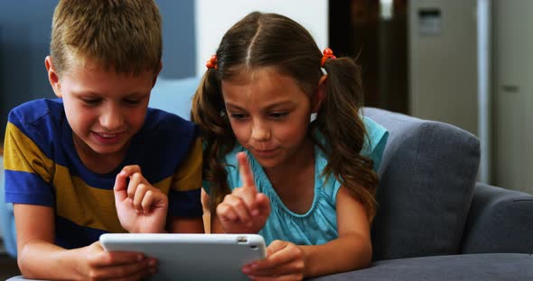 Siblings using digital tablet in living room