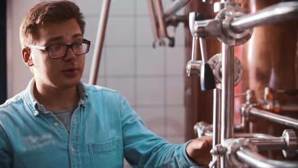 A Man Worker in Glasses at the Beer Factory Clings the Valves