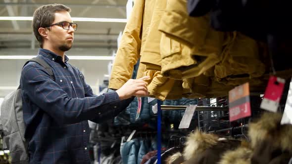 Adult Man is Looking and Touching Winter Jackets in a Sport Shop with Clothes