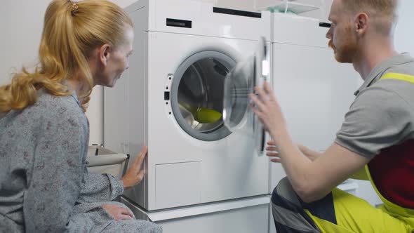 Young Service Man Installing New Washing Machine and Shaking Hands with Woman Client