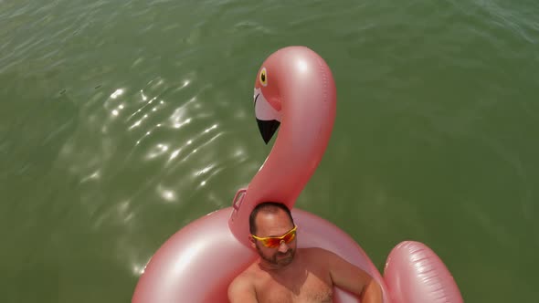 Man with yellow sunglasses taking selfie holding long stick and camera while relaxing on floating in