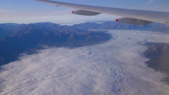 Aerial view of mountains and flying above clouds with view of airplane wing.