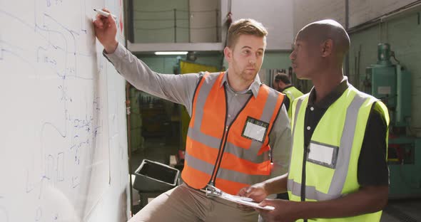 A Caucasian and an African American male factory worker holding a clipboards