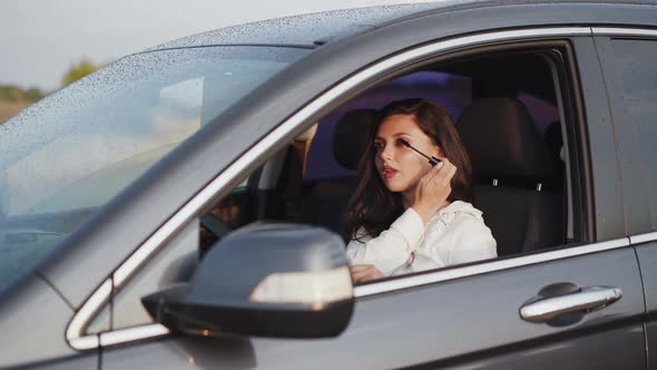 Brunette Applying Mascara to the Car Front Mirror and Smiling at Camera