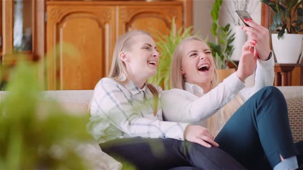 Two Positive Energetic Women Taking Selfie Photo on a Sofa in Luxury Modern Living Room