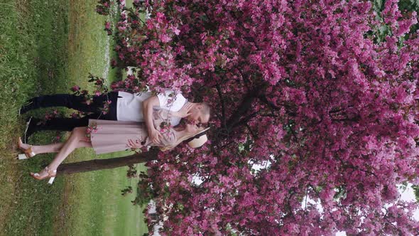 Romantic Beautiful Woman in a Hat Stands with a Man at a Cherry Blossom Tree in the Summer in the