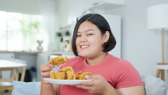Portrait of Asian young oversize big women eat unhealthy food, hold fried chicken and look at camera