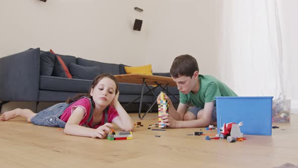 Girl and a boy playing and constructing with toy bricks on the living room floor