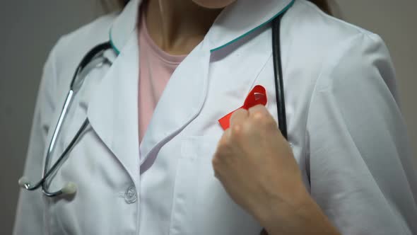 Female Doctor Attaching Red Ribbon to Medical Suit, AIDS Awareness Campaign