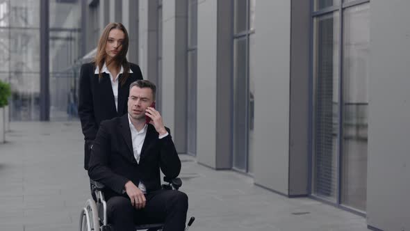 Crop View of Woman Pushing Wheelchair with Her Disabled Boss While Walking Near Office Building