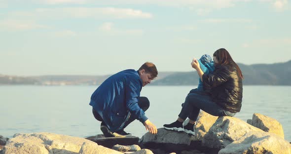 Man with His Family Sits on the Beach on Large Stones and Throws Stones Into the Water