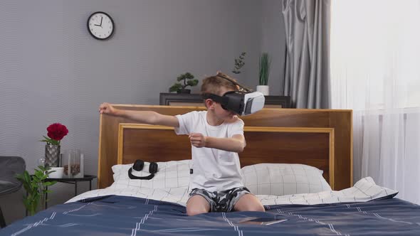 Positive Small Boy in Special 3d Glasses Playing Video Racing, Sitting on Bed in Bedroom